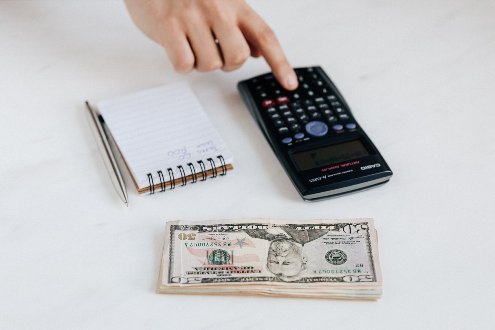 Person using calculator near notepad, pen, and pile of bills