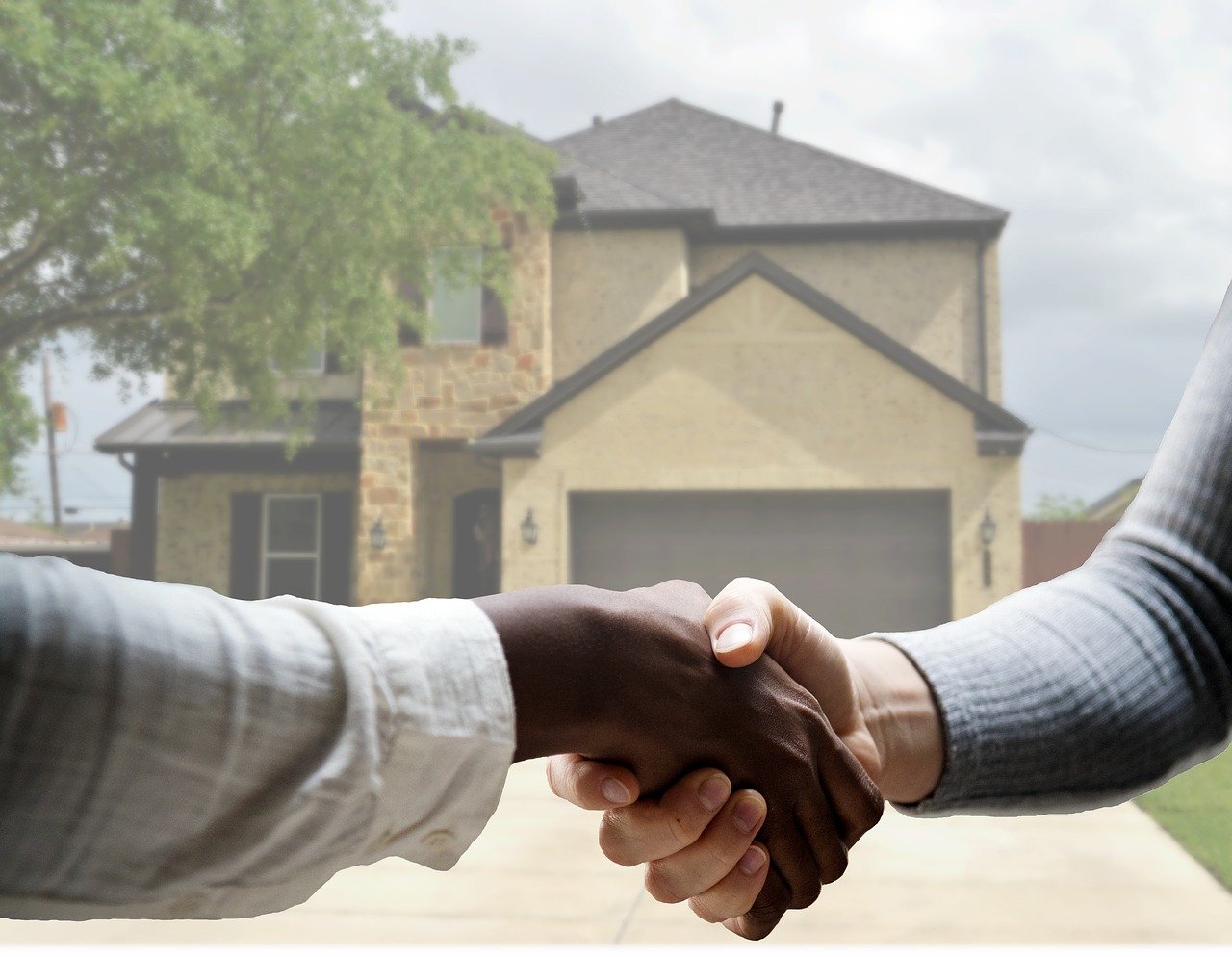 Two people shaking hands in front of house