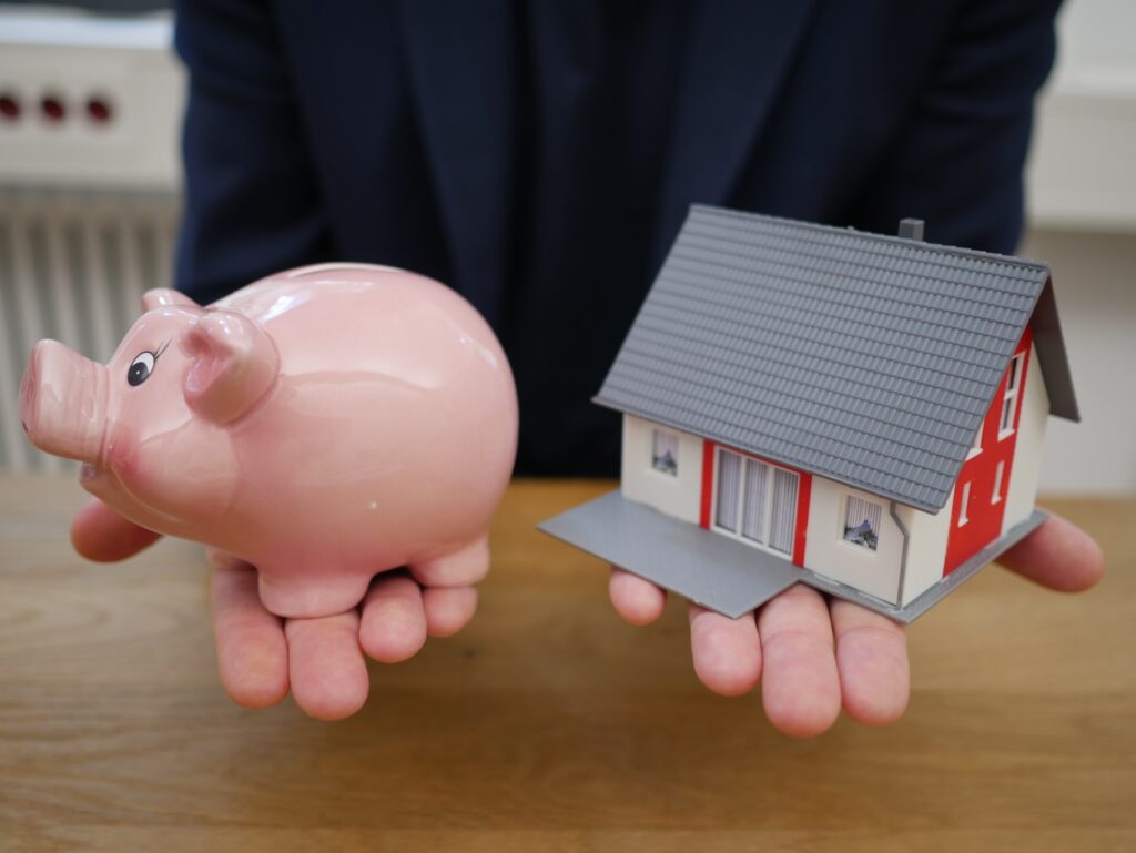 Person with a piggy bank and a small house model on the palms of his hands