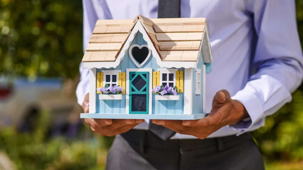 A real estate agent holding a miniature wooden house