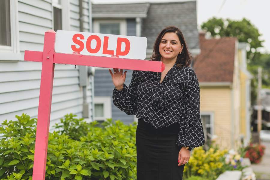 A real estate agent holding a sold sign in front of a house