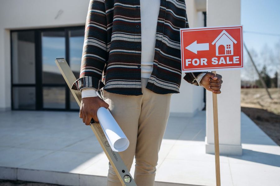 Person holding the for sale sign and papers in front of a new home