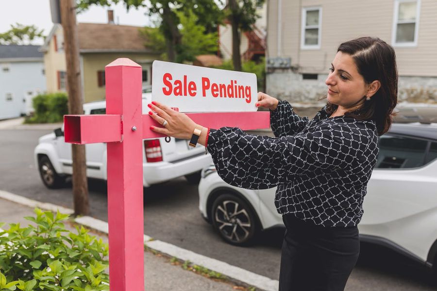 Real estate agent putting a Sale Pending sign on a house