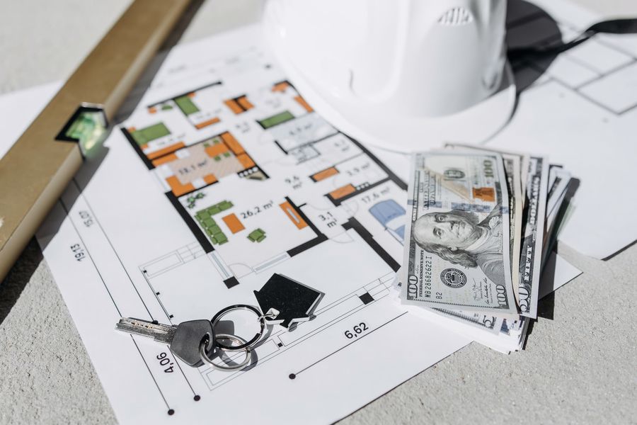 Floor plan, dollar bills and house key laid out on a table