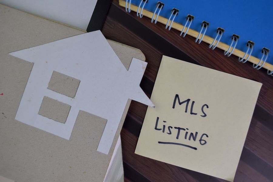 The word MLS Listing written down on a piece of paper, with a paper cutout of a house