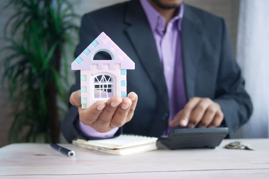 Person holding a toy house while pointing to a calculator