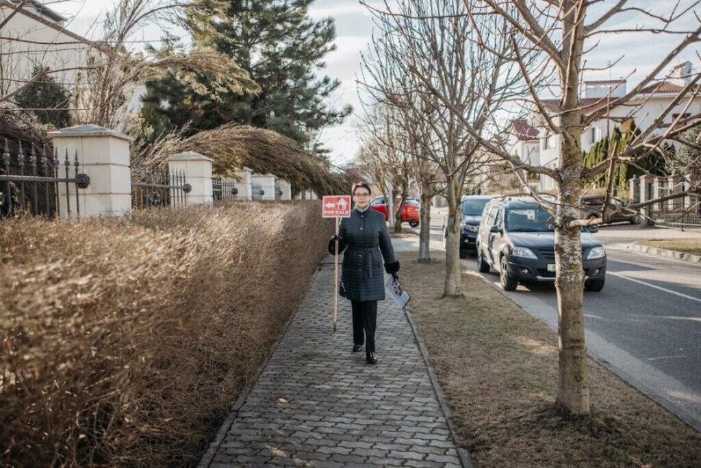 Real estate agent holding a For Sale sign while walking outside a property that is available for showing