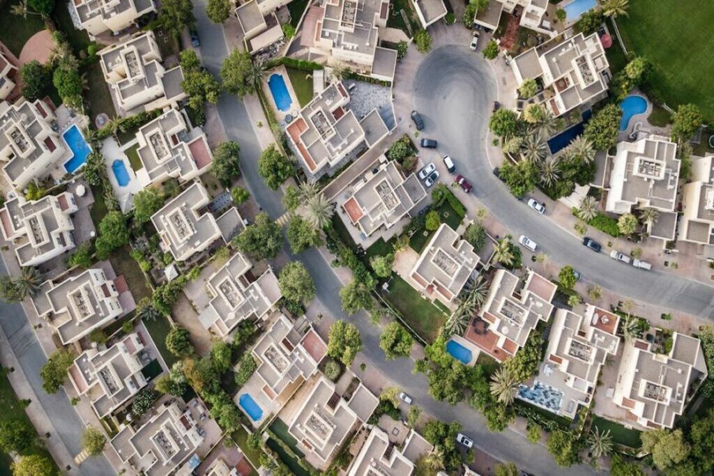 Overhead view of a diorama of a neighborhood, with uniformed white and gray roofs and miniature car models and green trees are placed around them