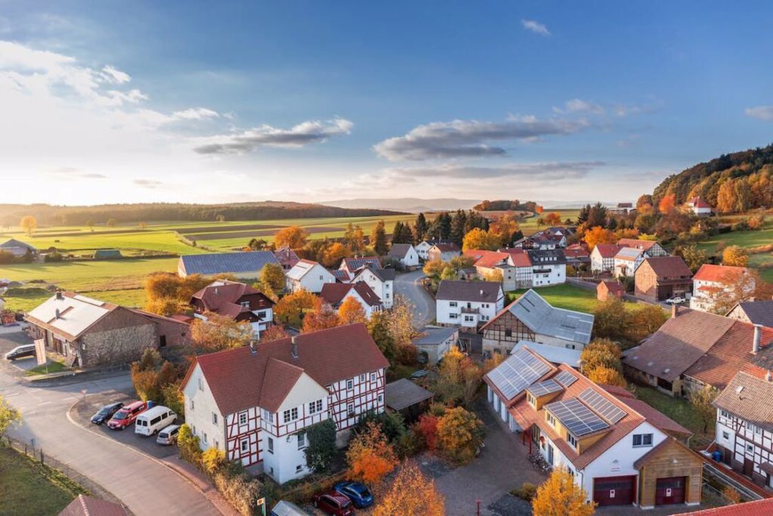 Overview of houses in a city with their red roofs visible above and an expansive green landscape behind them