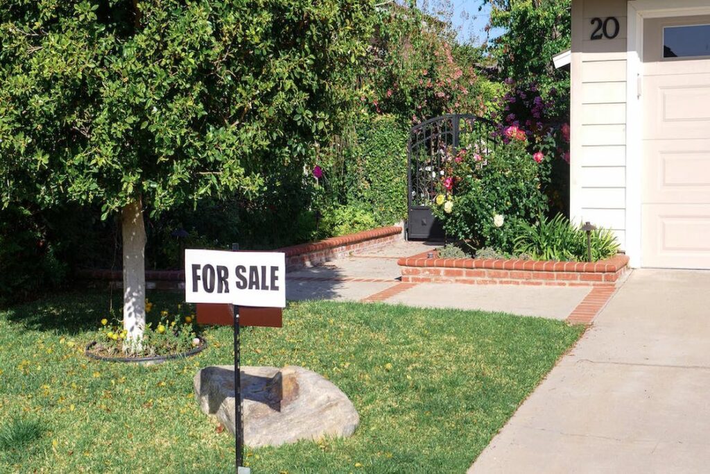 For Sale sign installed on a lawn grass in front of a house