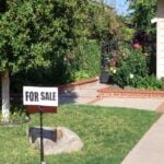 For Sale sign installed on a lawn grass in front of a house