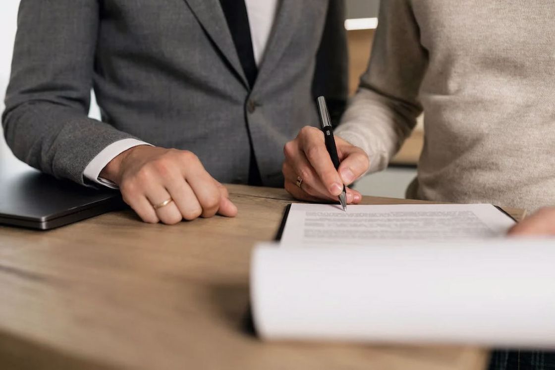 Person signing a document while a man wearing a suit looks on